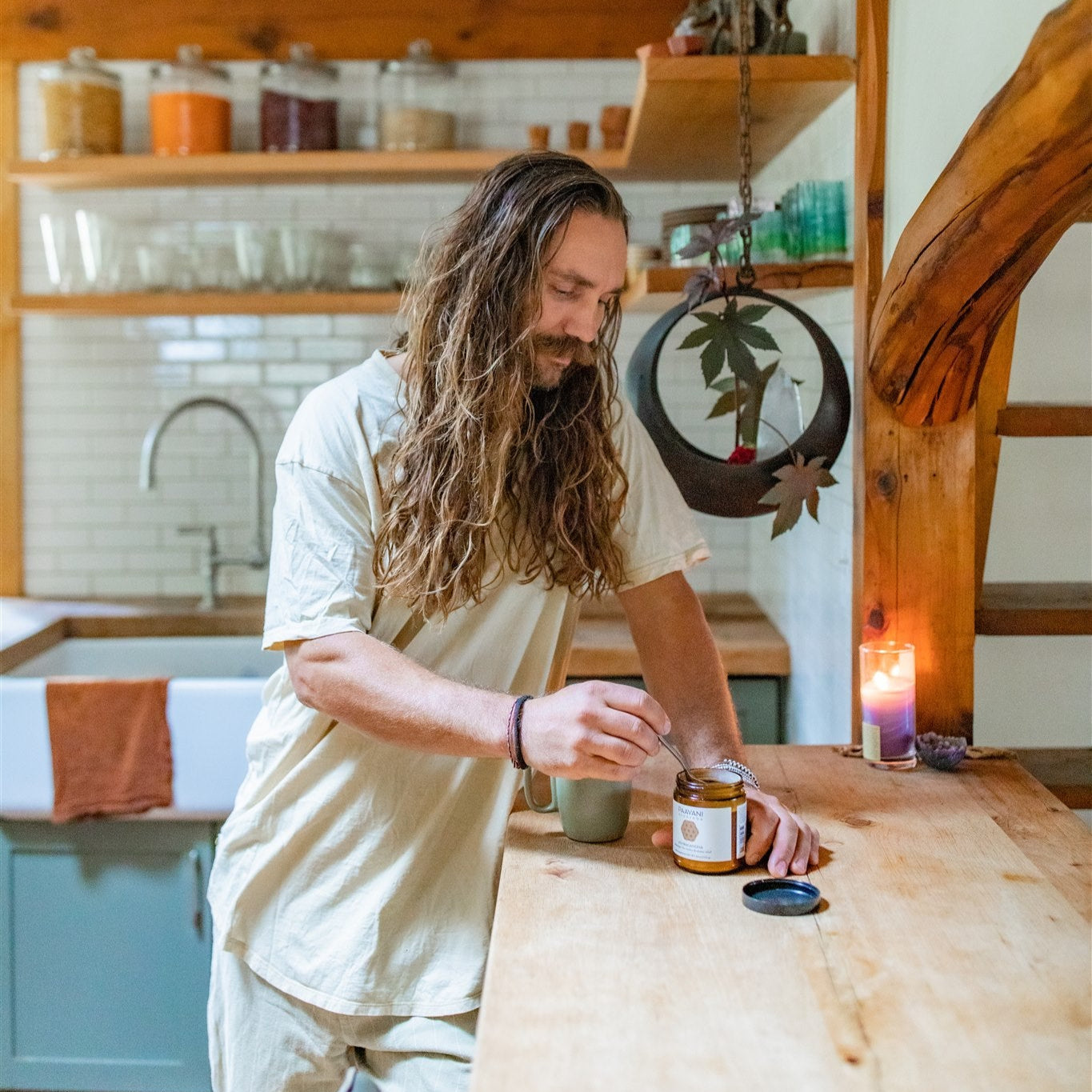 Man with long hair preparing a warm drink with PAAVANI Ayurveda Ashwagandha in a cozy, rustic kitchen setting.