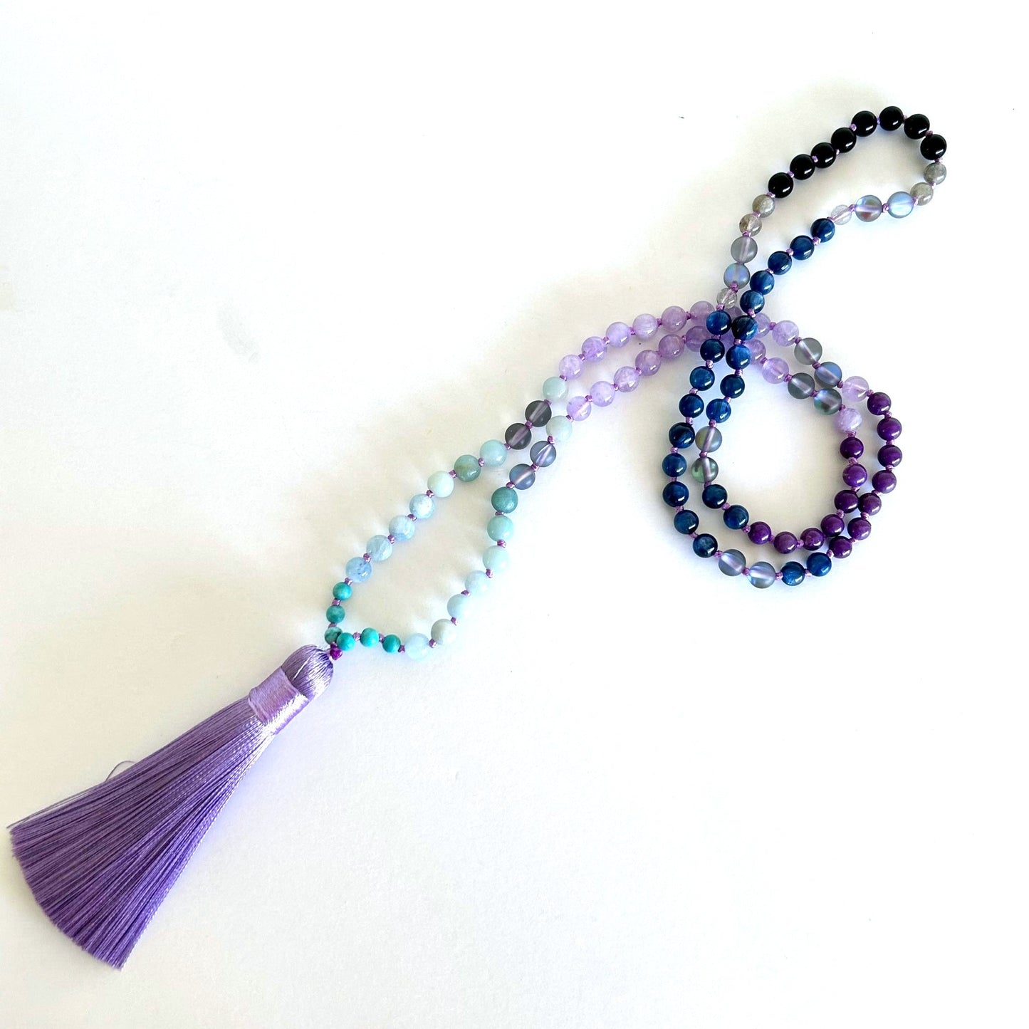 Mystic Mala necklace elegantly arranged on a white surface to highlight gradient gemstone colors