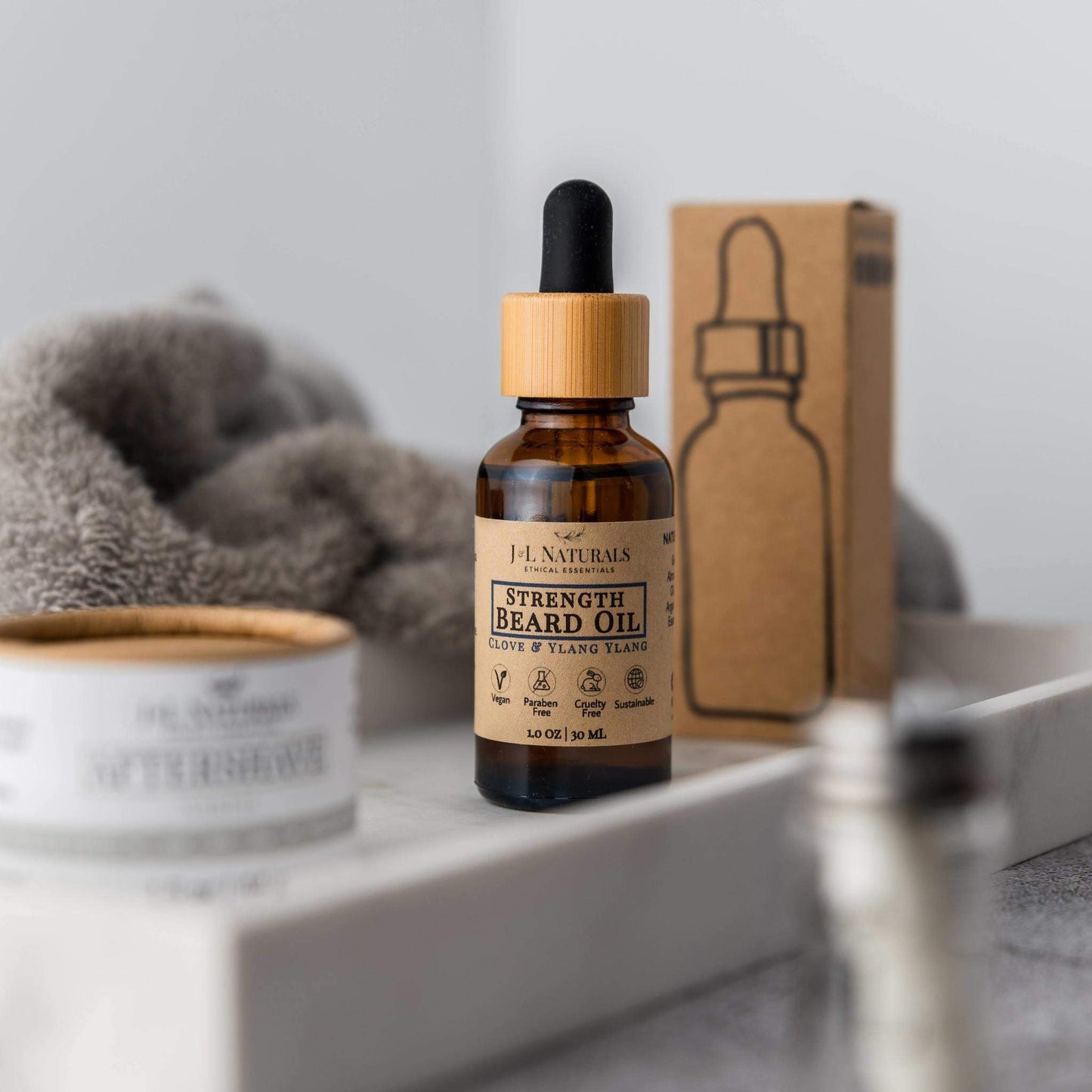 Strength Beard Oil by J&L Naturals displayed with eco-friendly packaging on a white tray, beside grooming essentials.