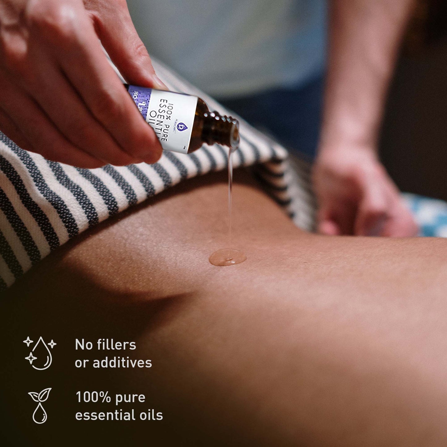 Hand pouring 100% pure essential oil onto a person’s back during massage, labeled with ‘No fillers or additives’ for clean, natural skincare.