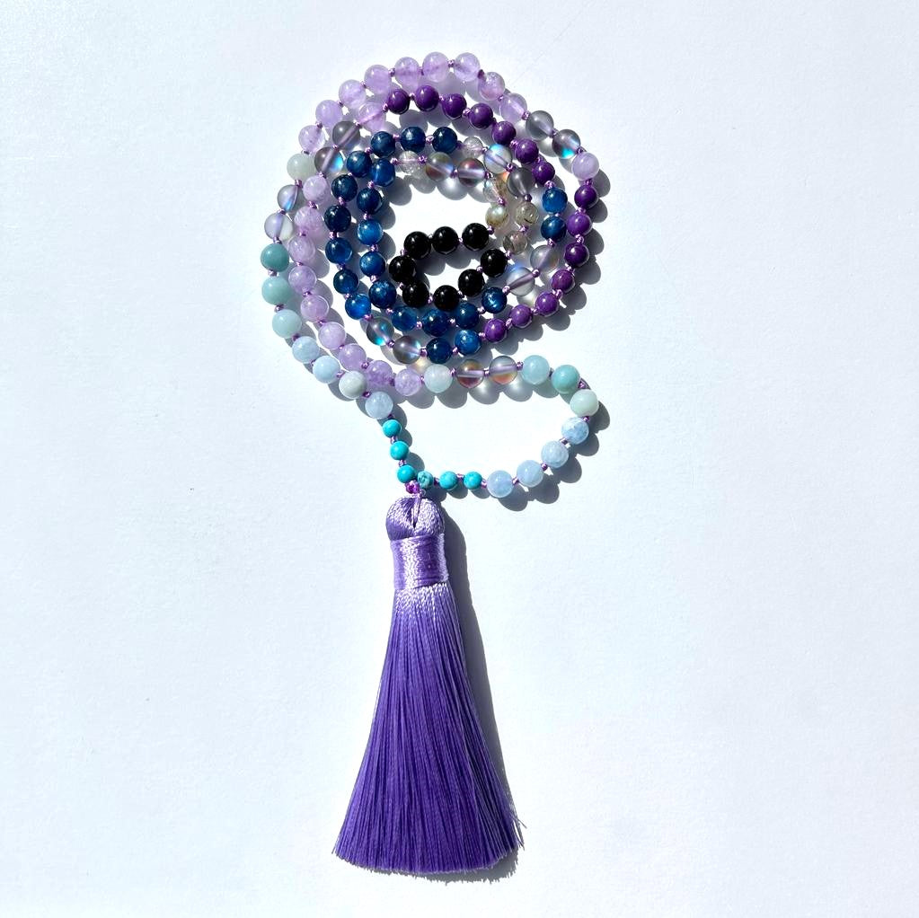 Mystic Mala necklace coiled in a spiral, showcasing beads of Kyanite Mystic, Aura Quartz, Sugilite, and Amazonite with a lavender tassel